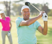 Portrait of cheerful mature golfer holding golf club while standing on field