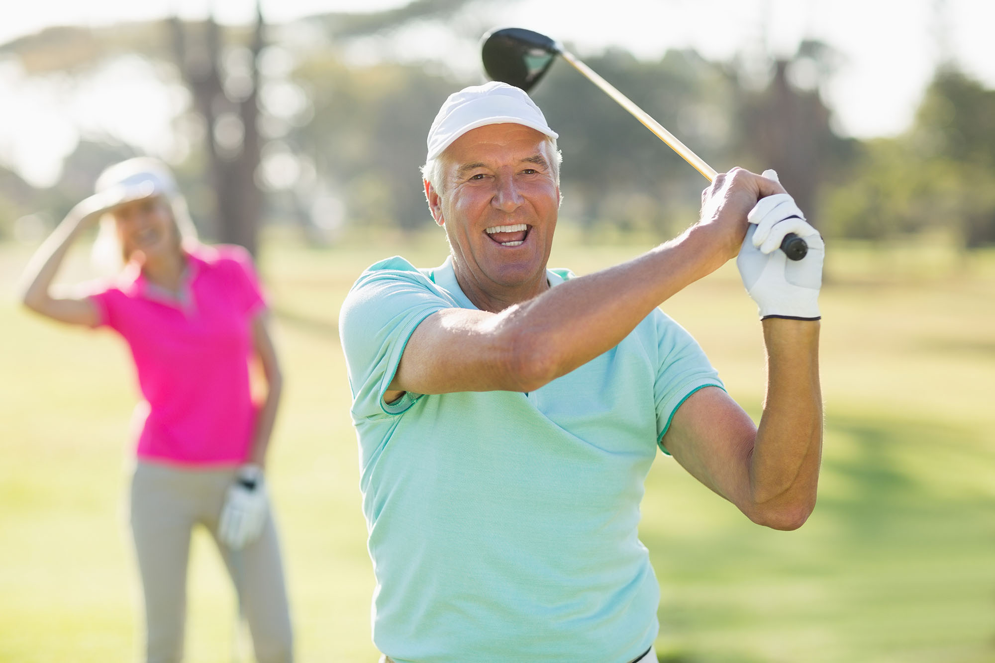 Portrait of cheerful mature golfer holding golf club while standing on field