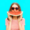 portrait happy young woman is holding slice of watermelon over colorful blue background