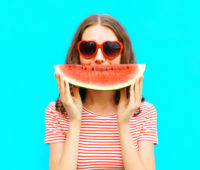 portrait happy young woman is holding slice of watermelon over colorful blue background