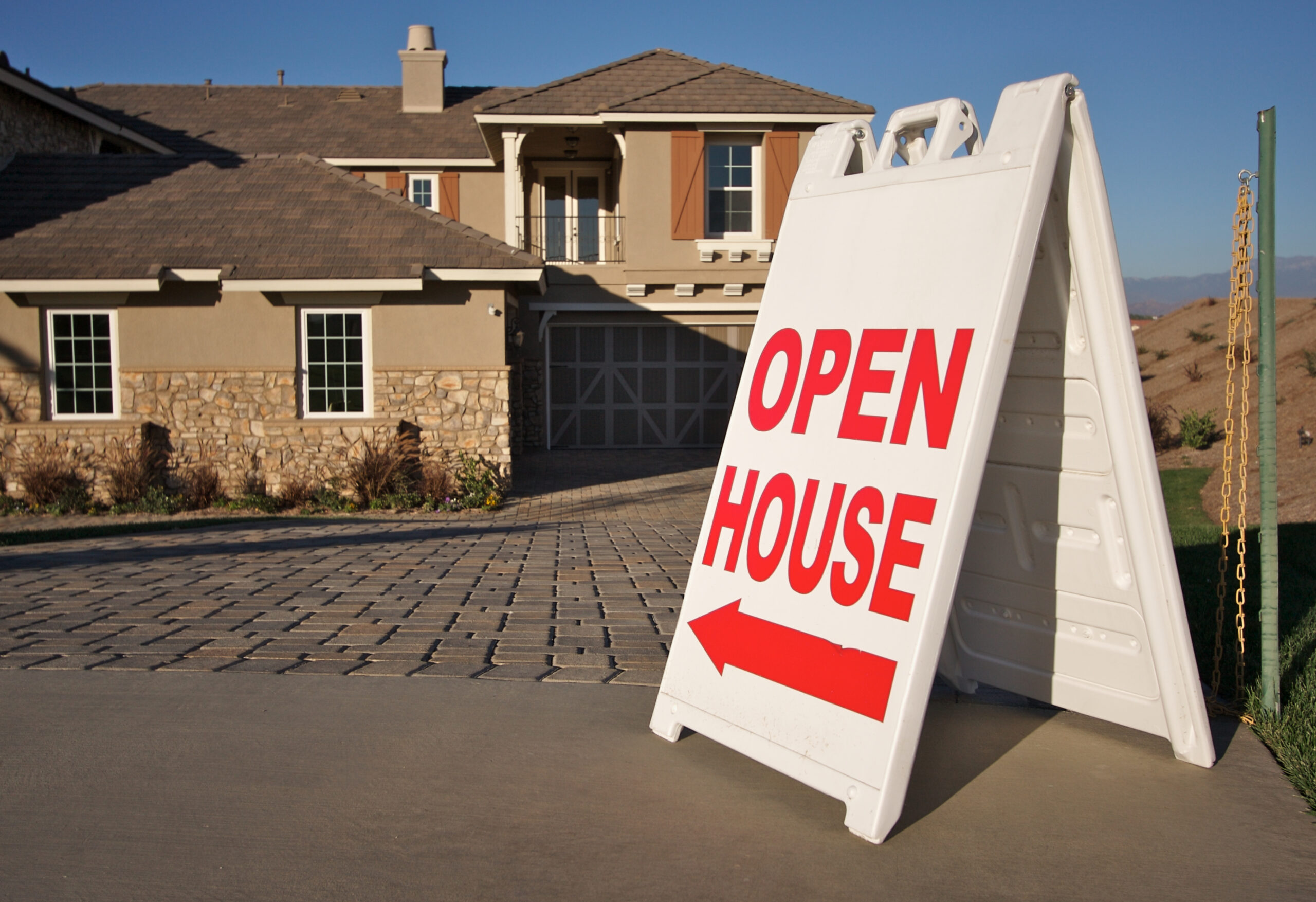 An open house sign in front of a tan-colored house.