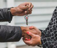 Two people shaking hands and exchanging a house key.