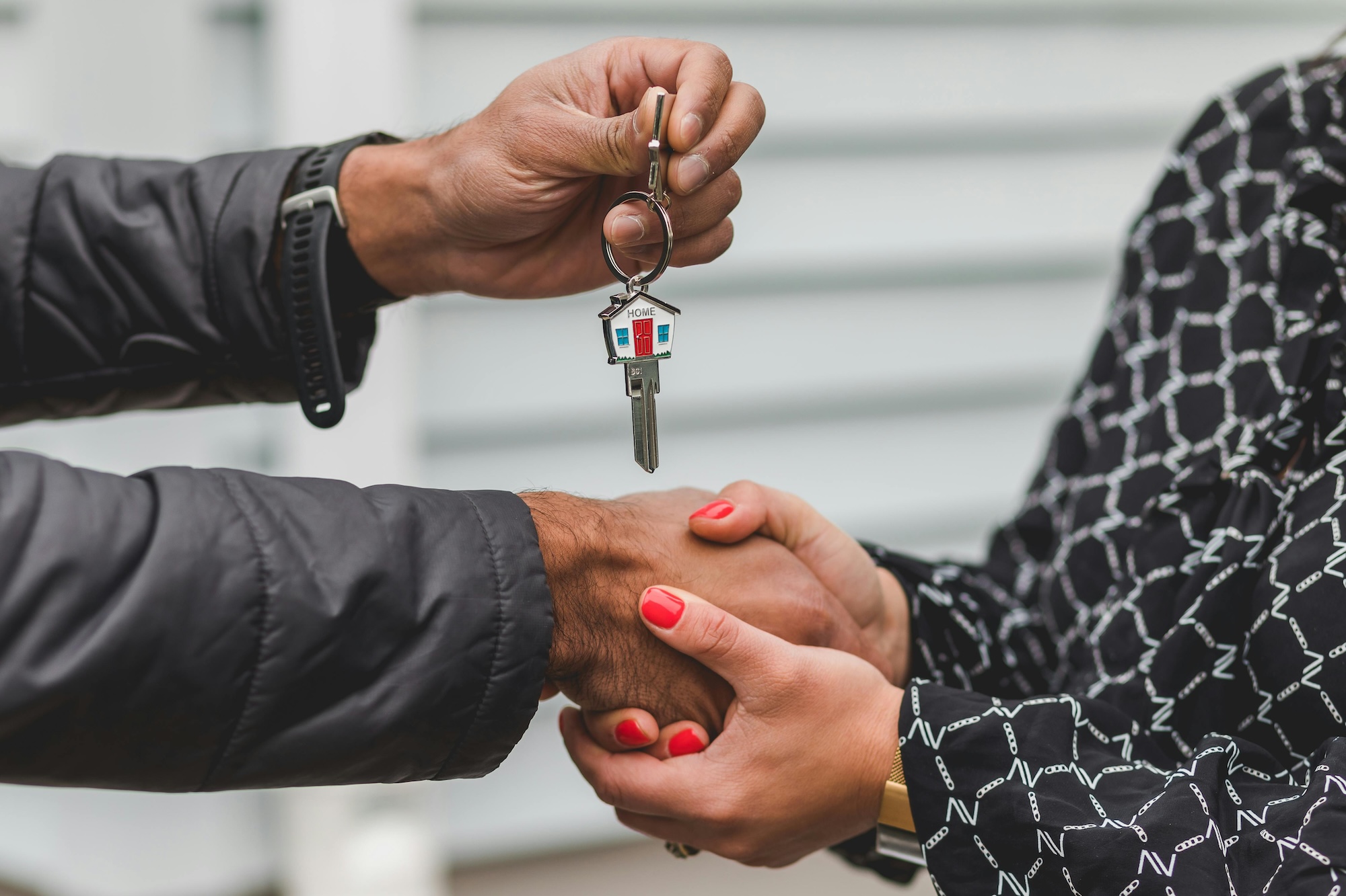 Two people shaking hands and exchanging a house key.