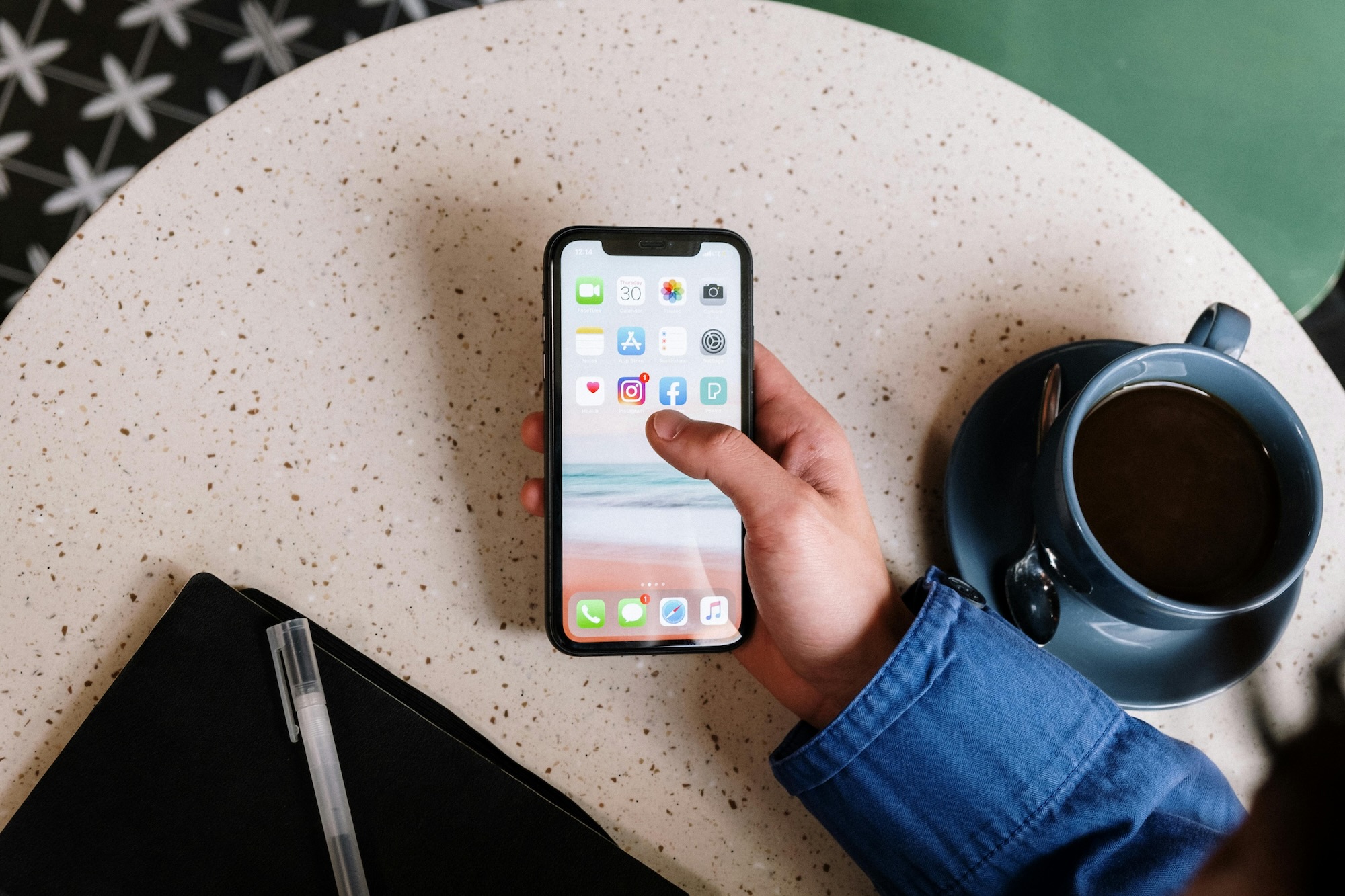 Person holding an iPhone with a mug next to them on the table.