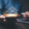 Hands holding a tablet with a glowing digital blueprint of a house overlayed, representing the integration of technology in modern real estate.