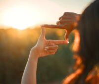 Hands forming a square frame gesture while capturing the setting sun, symbolizing a clear vision and future focus.