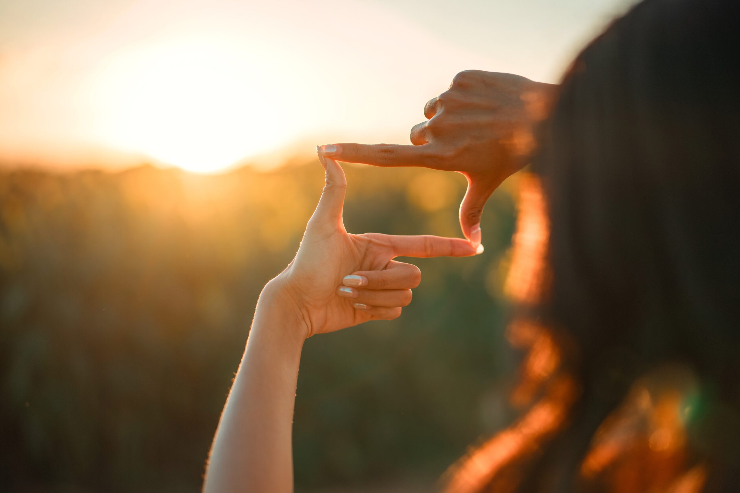 Hands forming a square frame gesture while capturing the setting sun, symbolizing a clear vision and future focus.