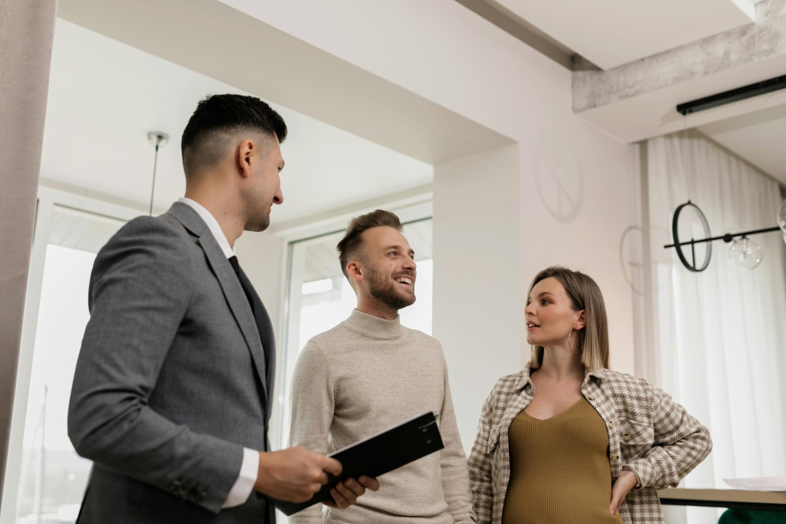 Couple standing next to a man in a suit inside a house.