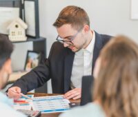 An agent sitting down and showing two people a piece of paper on a desk.