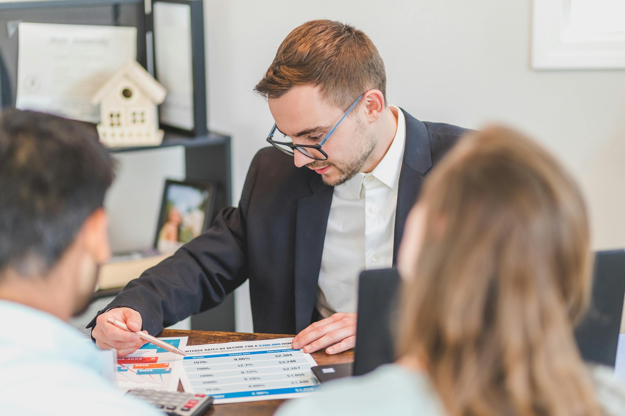 An agent sitting down and showing two people a piece of paper on a desk.